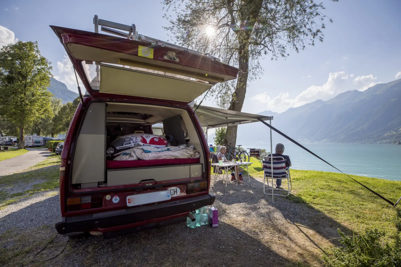 Ein Campingbus mit offener Heckklappe auf einem Seeplatz