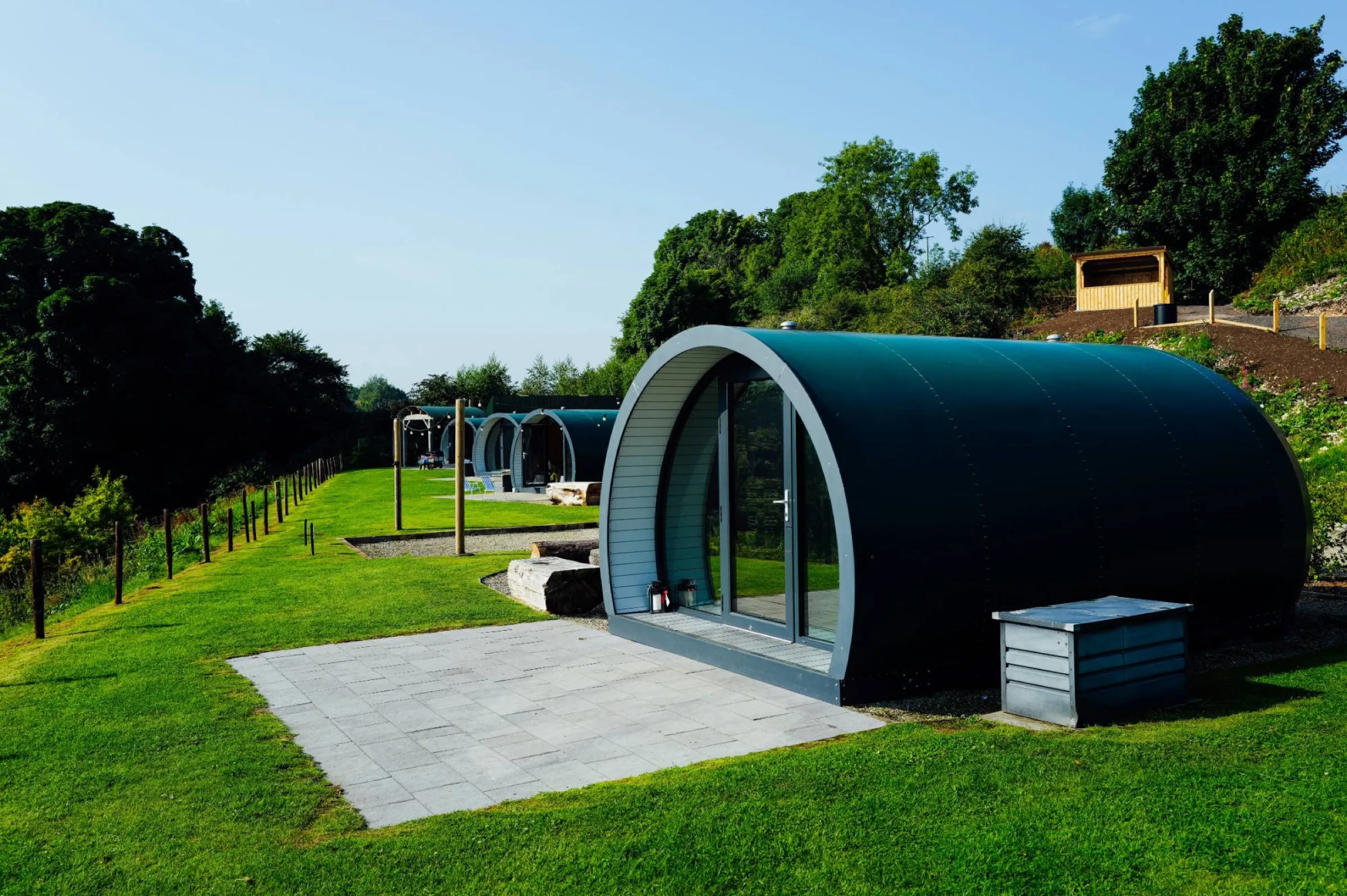 Dunkelgrüne, gewölbte Glamping-Pods auf einer sonnigen Wiese